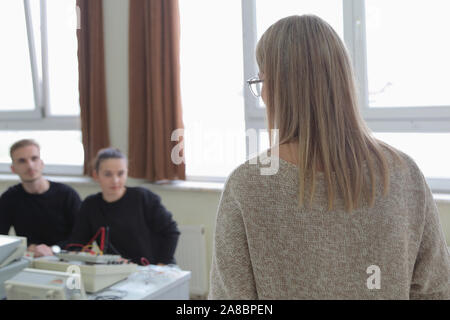 Two young students in technical vocational training with teacher, the lesson in technical college. Students with hands up. Education and technology co Stock Photo