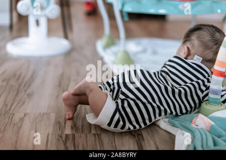 Adorable baby boy learning to crawl on the floor at home. Side view. Primary focus on baby feet. Stock Photo