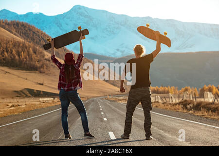 Couple of longboarders stands at straight mountain road with longboard above their heads. Outdoors longboarding concept Stock Photo