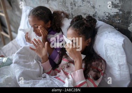 Two sisters lying in bed and sneezing after catching flu Stock Photo