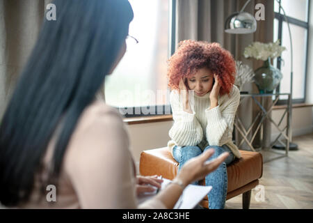 Woman having headache while speaking with psychologist Stock Photo