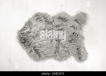 Flat lay view of gray warm and cozy whole decorative fake sheepskin shape rug on white wooden board floor.  Copy space, studio set. Stock Photo