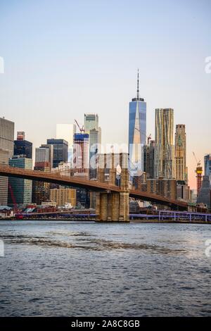 Brooklyn Bridge at sunrise, view from Main Street Park over the East River to the skyline of Manhattan with Freedom Tower or One World Trade Center Stock Photo