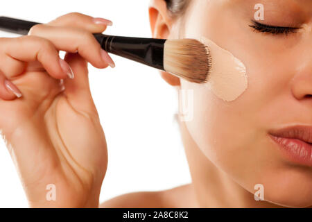A young woman applied liquid foundation on her face with a brush Stock Photo