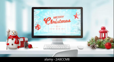 Christmas in office concept. Merry Christmas greeting on computer display. Christmas decorations on work desk. Stock Photo