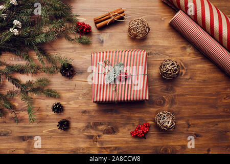Close-up of decorated Christmas present lying on the wooden table with branches of fir tree and wrapping papers around Stock Photo