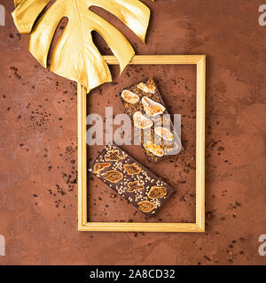Chocolate bars whole of various types of milky white dark framed golden leaf of a monstera plant on a brown textured background. Flat top view. Copy s Stock Photo