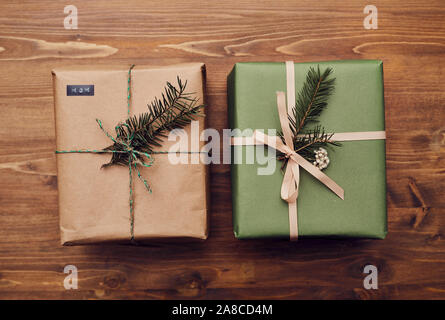 Close-up of two Christmas presents wrapped in wrapping papers decorated with fir branches on the wooden table Stock Photo
