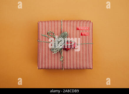 Close-up of Christmas gift box decorated with fir branch and red berries wrapped in striped wrapping paper isolated on yellow background Stock Photo