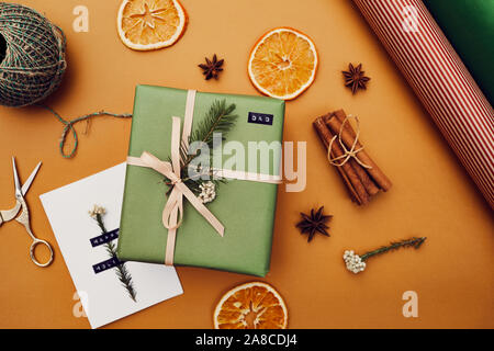 Close-up of decorated gift box in green wrapping paper with handmade greeting card lying among dried orange isolated on yellow background Stock Photo