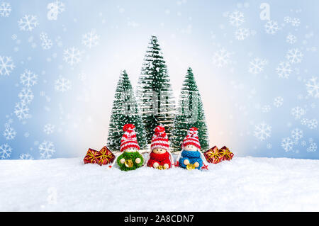 Knitted dolls as small children in colorful sweaters holding bells near fir trees and presents. Cute Christmas figures as a handmade holiday decoratio Stock Photo