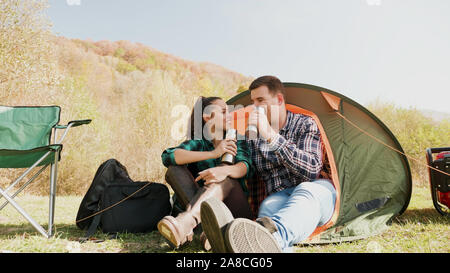 Couple enjoying a drink together in front of their camping tent. Camping chairs. Camping generator. Stock Photo
