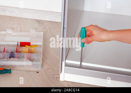 Repairs in house or apartment. Female hand repairing white furniture with a screwdriver in home, close up. Diy concept. Stock Photo