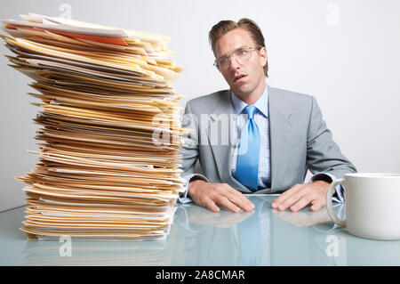 Businessman looking overwhelmed by the stack of paperwork on his desk Stock Photo