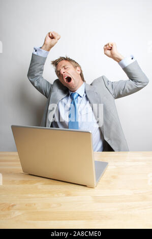 Tired businessman yawning at his desk with his arms in the air Stock Photo