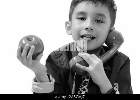 Cute boy sticking tongue out while holding green apple and talking on old telephone Stock Photo