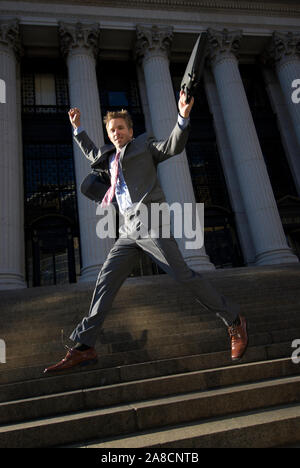 Excited lawyer businessman jumping on dark steps with grand courthouse columns in the background Stock Photo