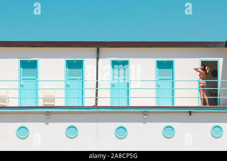 A young woman in a bikini combs her hair outside vintage bathing cabins in Viareggio, Tuscany, Italy. Stock Photo