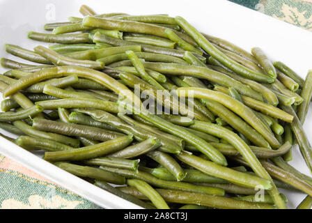 Homemade cooked string green beans served in a white casserole dish. The background is a Thanksgiving Autumn themed tablecloth. Stock Photo