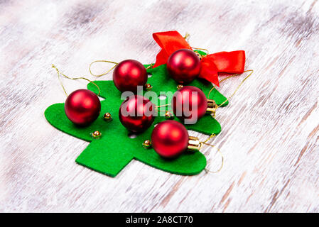 On a wooden table lies a felt Christmas tree made by hands with red balls and a red bow at the top. Christmas Craft Stock Photo