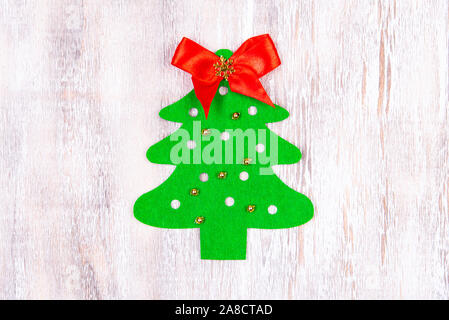 A felt christmas tree made by hands with golden bead toys and a red bow at the top lies on a wooden table. Christmas Craft Stock Photo