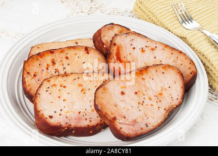 Homemade boneless smoked pork chops covered with assorted herbs and spices. An antique linen tablecloth is in the background. Shot in natural light. Stock Photo