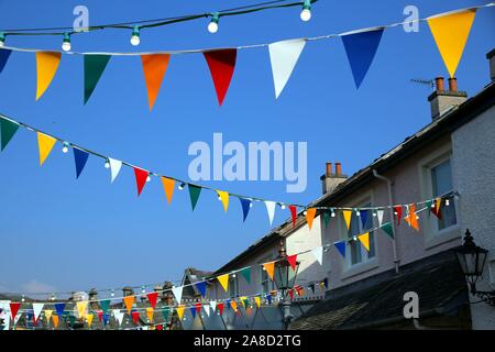 Bright colorful bunting or pennant flags hanging across pretty village street against blue sky for a traditional celebration, multi coloured. Stock Photo