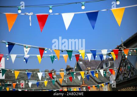 Bright colorful bunting or pennant flags hanging across pretty village street against blue sky for a traditional celebration, multi coloured. Stock Photo