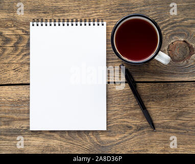 Open notebook on a spring with a white paper for notes and drawing near a pencil and a mug of tea. Background distressed wood, top view. Stock Photo