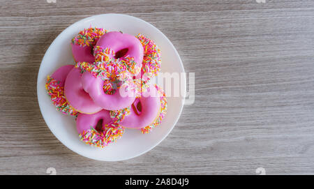 Pink glazed mini donuts in white plate on wooden table. Sweet food background Stock Photo