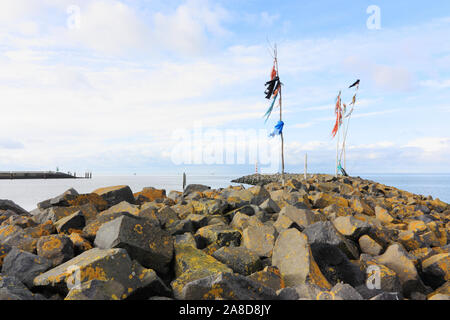 Poles with colored rope and plastic waving in the wind on breakwater or pier in the Wadden Sea at the entrance to the port of Harlingen The Netherland Stock Photo