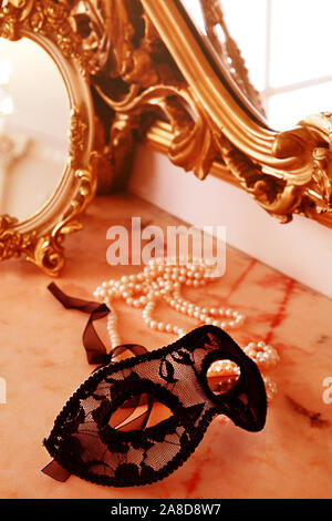 Black lace masquerade mask on table. Female Boudoir, pearl necklace, mirror, mask Stock Photo