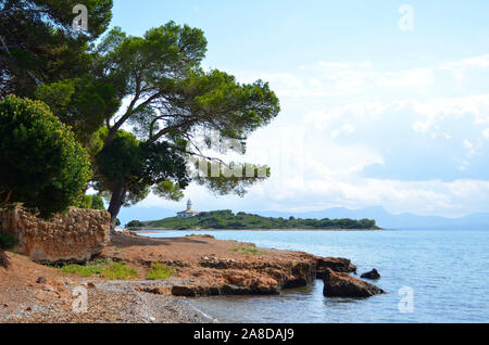 Islet with the lighthouse near the port of Alcudia. Pine trees in the foreground with the island of Alcanada in the background. Stock Photo