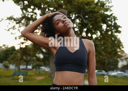 Portrait of a fit young black woman stretching her neck in the park before doing exercise outdoors