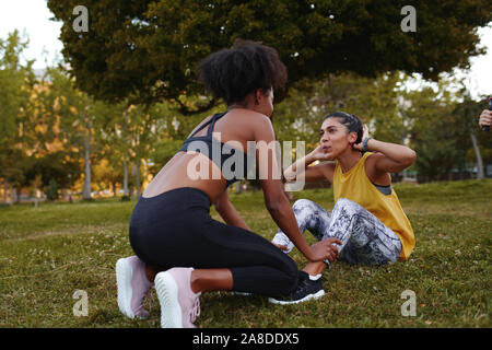 Fit young woman doing crunches exercise with her female friends during athlete workout in the park - young determined and motivated woman doing Stock Photo