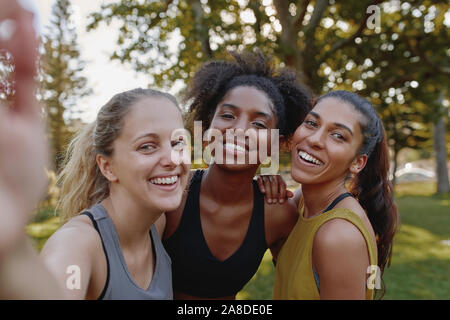 Smiling portrait of diverse female friends looking at camera taking selfie in park - fitness friends taking a selfie after exercising  Stock Photo