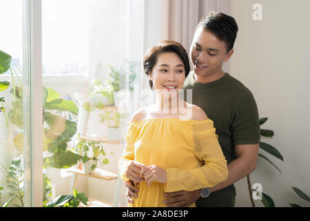 Happy man and woman hugging and standing near window at home together Stock Photo