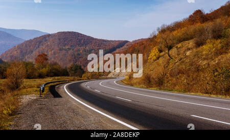 Empty curving tarred road with crash barrier passing through mountains under a clear sunny blue sky in a rural landscape Stock Photo