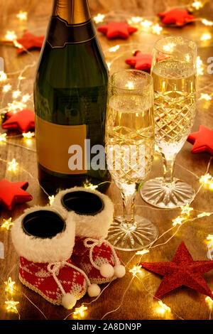 Champagne flutes and bottle with christmas lights, baubles and red stars decorations, on a wooden table Stock Photo