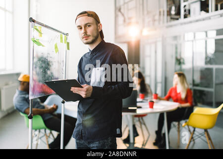 Young team of coworkers making great meeting discussion in modern coworking office. Portrait of creative professional looking over a post it note wall Stock Photo