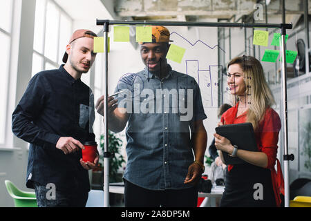Three young Business people meeting at office and use post it notes to share idea. Brainstorming concept. Sticky note on glass wall. Stock Photo
