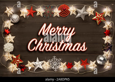 Merry Christmas words surrounded by a  border of golden star christmas lights and sparkling christmas decorations, on a distressed dark wooden board b Stock Photo