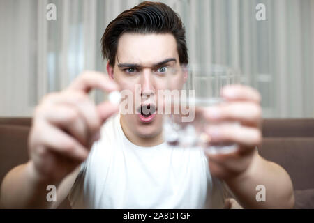 young man holding pill and glass of water suffering headache after partying handover. Stock Photo