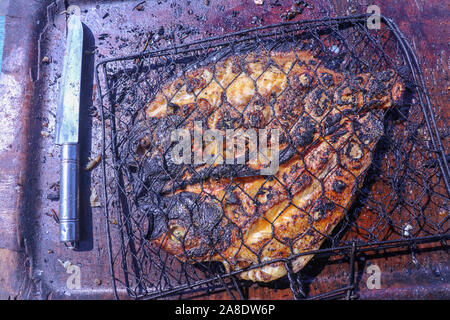 Barbeque made of seafood. Grilled Snapper coral fish with delicate Balinese salsa. Halved fish in barbecue grill. Healthy food on brown tray. Stock Photo