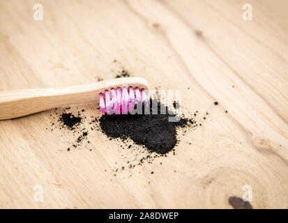 Raw activated charcoal powder on wooden background natural bamboo toothbrush inside it. Charcoal toothpaste concept. Minimalist composition with lot o Stock Photo