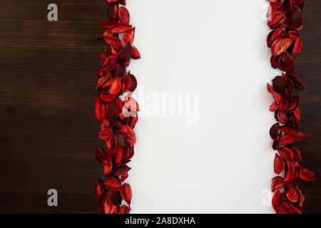 Flat lay Christmas copy space with dark wood on one side and red petals bordering a white background Stock Photo