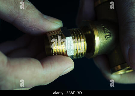Plumber hands screwing nut of pipe over plumbing tools background. Concept of repair and technical assistance. Close up shot. Brutal atristic toning. Stock Photo