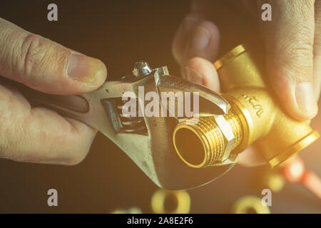 Plumber hands screwing nut of pipe over plumbing tools background. Concept of repair and technical assistance. Close up shot. Brutal atristic toning. Stock Photo