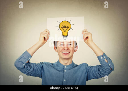 Smiling teenager boy holding a paper sheet with a lightbulb sketch above his head. Education and genius concept, science and business ideas and planni Stock Photo