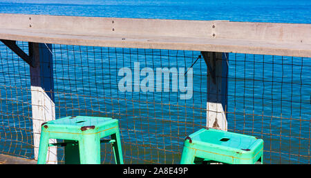 Green metal stool with handle hole. Wooden pier railing on the blue waterfront. Concept or symbol -  vacation, travel, and relaxation Stock Photo